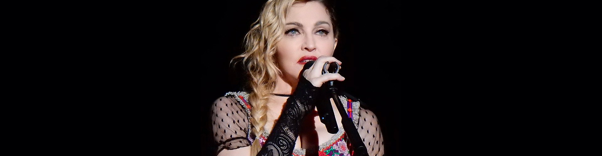 Color photograph of Madonna singing against black background on Ronnie Stangler MD media and events page regarding article by Dr. Stangler in Horizons Family Office and Investor Magazine by Opalesque, What Does Madonna Know About Her Genes That You Don't?