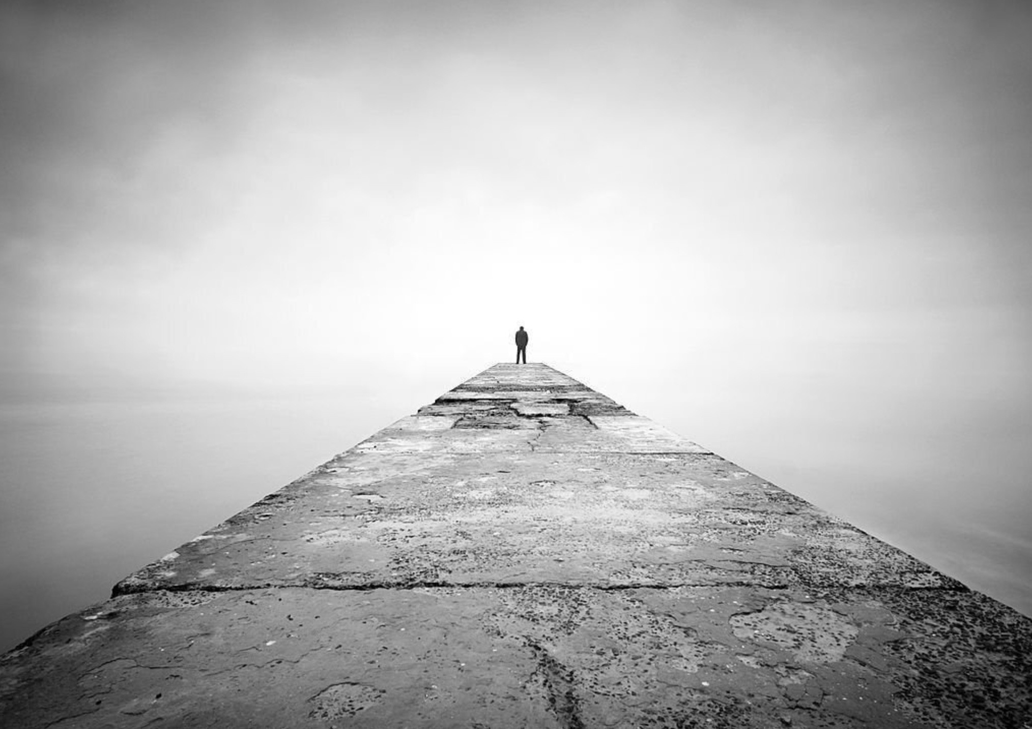 Black and white photograph man standing at edge of long pier in Ronnie Stangler MD good reads page regarding Eight Key Social Factors in Longevity